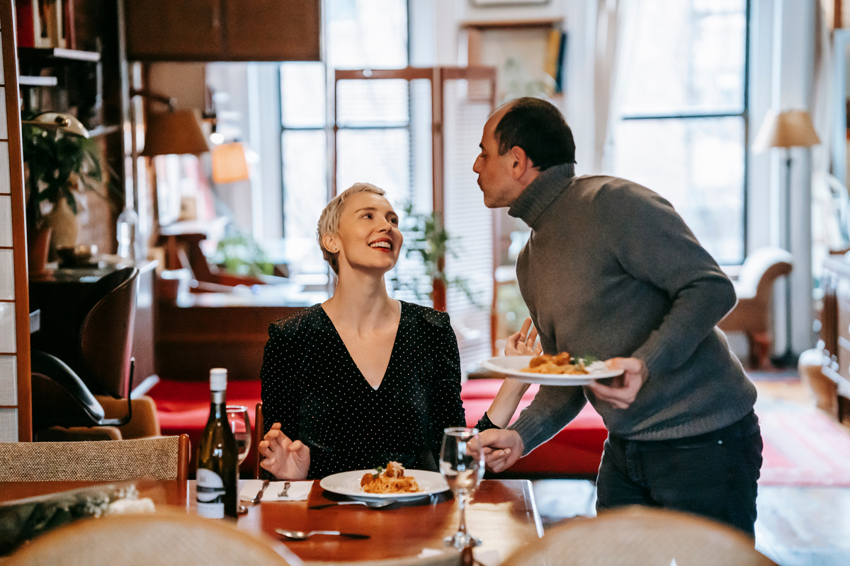 Positive couple having dinner with pasta at restaurant